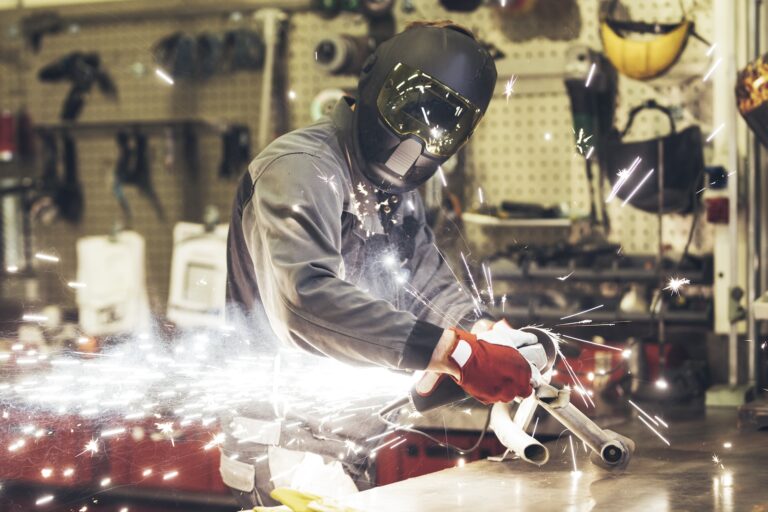 Metal worker in mask cutting pipes with sparks flying around